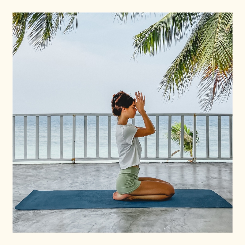 A woman practicing yoga in a yoga shala in front of the turquoise ocean in Thailand.