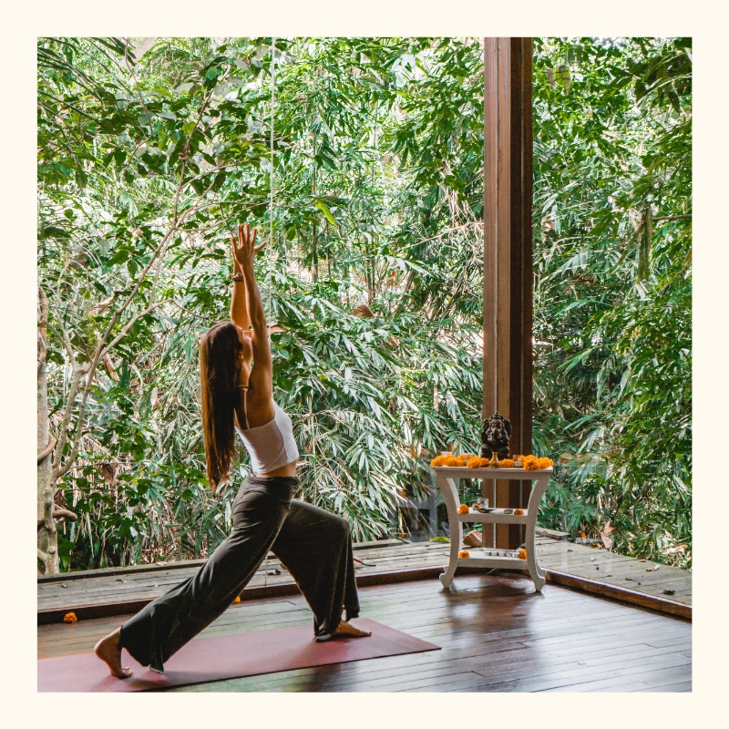 A woman practicing yoga in the shala of the yoga studio Radiantly Alive in Ubud surrounded by a lush jungle.