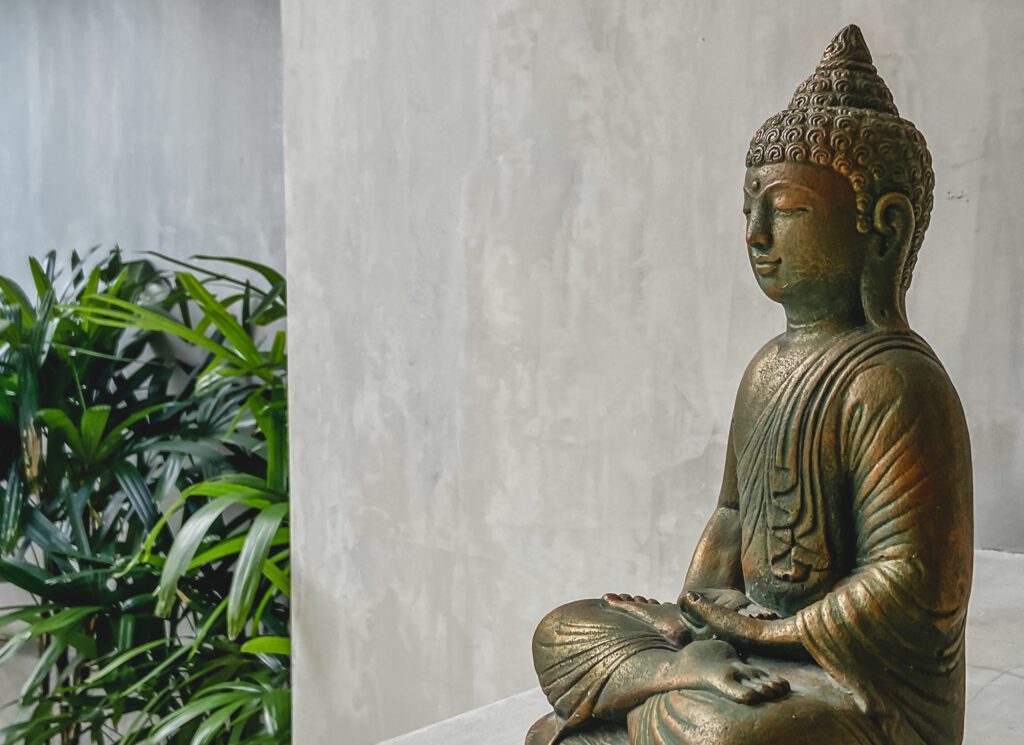 A bronze buddha statue in front of a simple white wall.