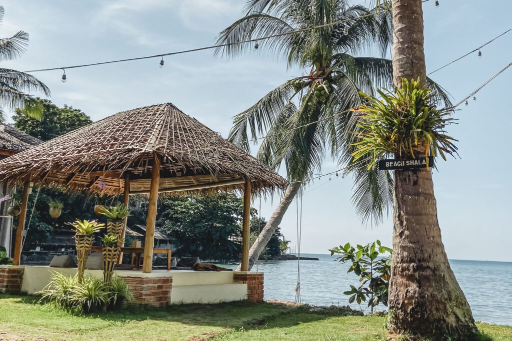A tropical, secluded bay in retreat of yoga in Thailand with a little bamboo hut and palm trees in front of the blue ocean.